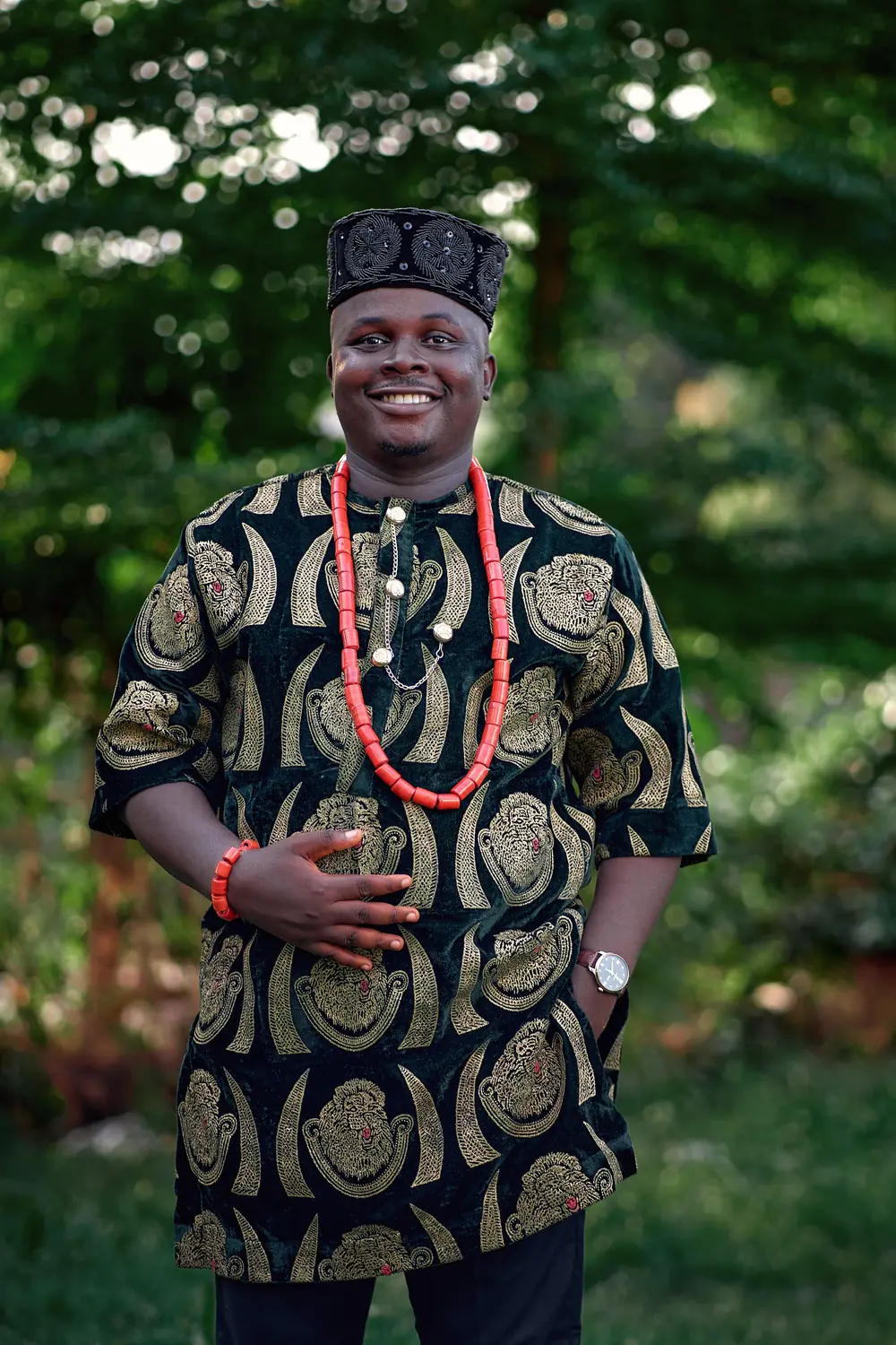 A smiling man in a black and gold isiagu with coral beads